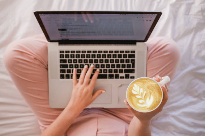 woman holding a cup of coffee and using Our-Venue.co.uk on a laptop